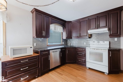 The kitchen features dark wood cabinetry, granite countertops, and a tile backsplash - 11815 76 Avenue, Edmonton, AB - Indoor Photo Showing Kitchen