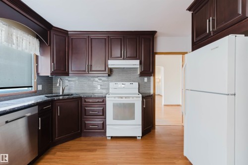 The kitchen features dark wood cabinetry, a stainless steel dishwasher, and a white oven with an overhead range hood - 11815 76 Avenue, Edmonton, AB - Indoor Photo Showing Kitchen