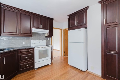 The kitchen features dark wood cabinetry, a white electric range, and a white refrigerator - 11815 76 Avenue, Edmonton, AB - Indoor Photo Showing Kitchen