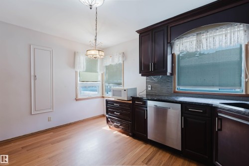 This kitchen features hardwood floors, dark wood cabinetry, and a stainless steel dishwasher - 11815 76 Avenue, Edmonton, AB - Indoor Photo Showing Kitchen