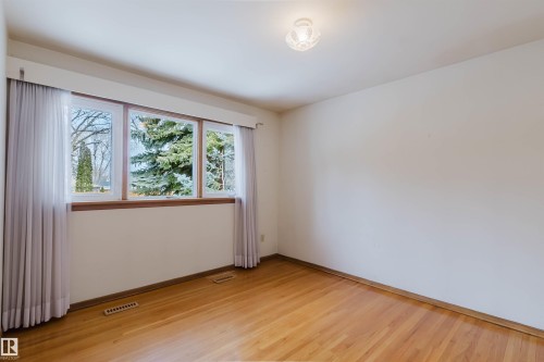 This room features hardwood flooring, white walls, and a multi-pane window with a wood frame, offering views of mature trees - 11815 76 Avenue, Edmonton, AB - Indoor Photo Showing Other Room