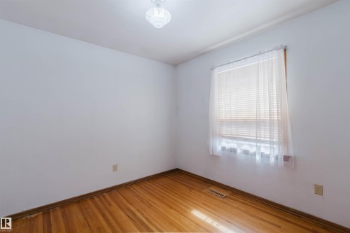 This room features hardwood floors, a window with blinds and sheer curtains, and a ceiling light fixture - 11815 76 Avenue, Edmonton, AB - Indoor Photo Showing Other Room