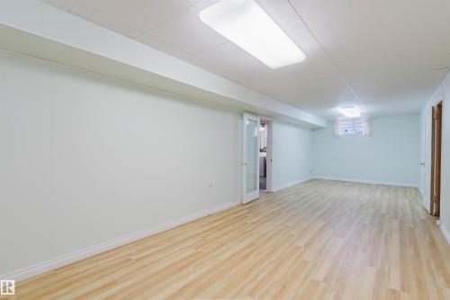 Bright and expansive room featuring light wood-style flooring, a drop ceiling with recessed lighting, and a window for natural light - 11815 76 Avenue, Edmonton, AB - Indoor