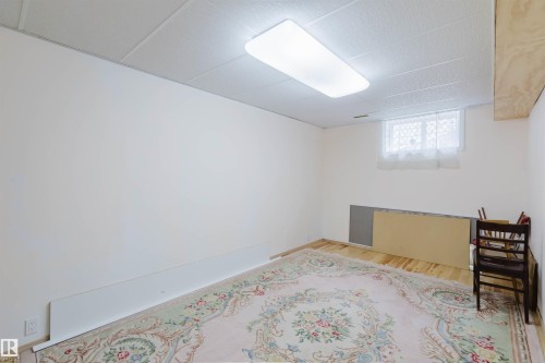 This room features light-toned flooring, a patterned area rug, and a window with white curtains - 11815 76 Avenue, Edmonton, AB - Indoor Photo Showing Other Room