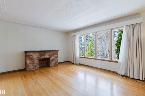 This room features hardwood floors, a brick fireplace, and large windows providing views of the outdoors - 11815 76 Avenue, Edmonton, AB - Indoor With Fireplace