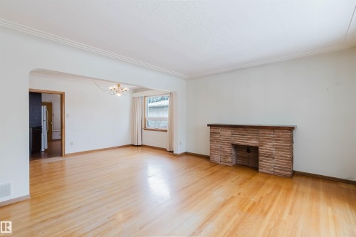 Spacious room featuring hardwood floors, a brick fireplace, a window with curtains, and crown molding - 11815 76 Avenue, Edmonton, AB - Indoor
