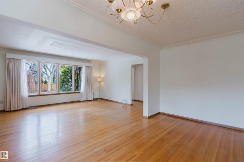 Open-concept living area featuring hardwood flooring, a large window with views of trees, and an ornate ceiling fixture - 11815 76 Avenue, Edmonton, AB - Indoor Photo Showing Other Room