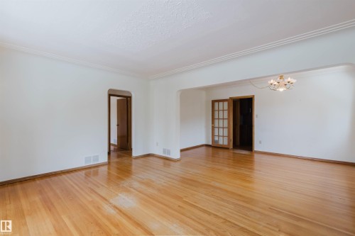 Spacious room featuring hardwood floors, white walls, and a decorative ceiling light fixture - 11815 76 Avenue, Edmonton, AB - Indoor Photo Showing Other Room