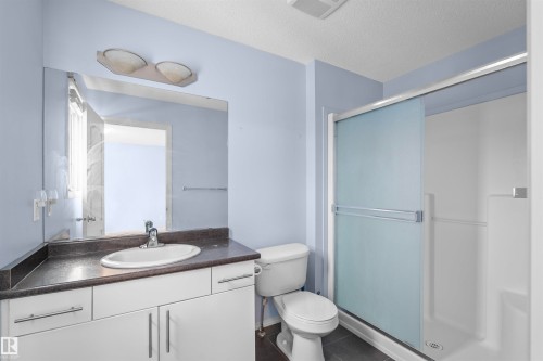 The bathroom features a vanity with a dark countertop and white cabinetry, a toilet, and a stand-up shower with frosted sliding glass doors - 11542 18A Avenue, Edmonton, AB - Indoor Photo Showing Bathroom