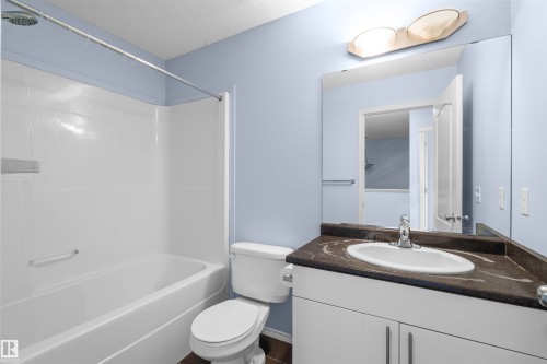 Bathroom featuring a white bathtub and shower combination, a toilet, and a vanity with a dark countertop and white cabinetry - 11542 18A Avenue, Edmonton, AB - Indoor Photo Showing Bathroom