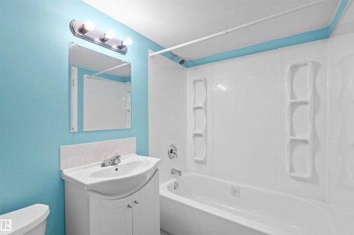 Bathroom featuring a vanity with a white basin sink, a mirror with an overhead light fixture, and a white bathtub with integrated shelving - 11542 18A Avenue, Edmonton, AB - Indoor Photo Showing Bathroom