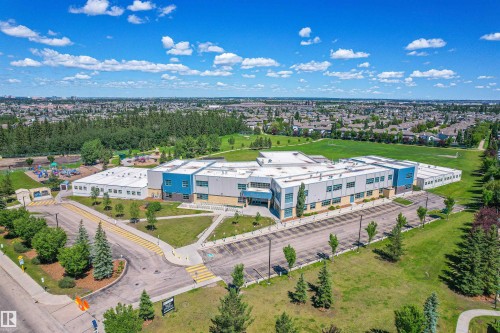 Aerial view showcasing a modern building with blue and grey accents, surrounded by green spaces and residential neighborhoods - 11542 18A Avenue, Edmonton, AB - Outdoor With View