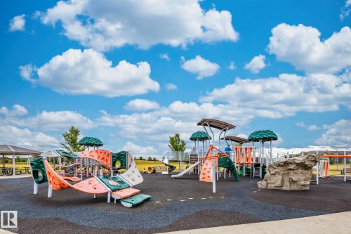 The property provides access to a vibrant playground area featuring various climbing structures, slides, and a rock climbing wall, all set on a dark-colored soft surface - 11542 18A Avenue, Edmonton, AB - Outdoor With View