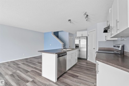 Kitchen featuring white cabinetry, stainless steel appliances, an island with an integrated sink and dishwasher, and dark countertops - 11542 18A Avenue, Edmonton, AB - Indoor Photo Showing Kitchen
