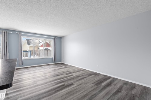 This living area features light-colored walls and grey-toned wood-style flooring - 11542 18A Avenue, Edmonton, AB - Indoor