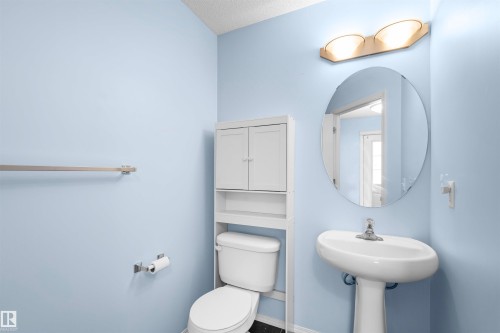 The bathroom features a pedestal sink with a circular mirror, a toilet, and a white storage cabinet - 11542 18A Avenue, Edmonton, AB - Indoor Photo Showing Bathroom