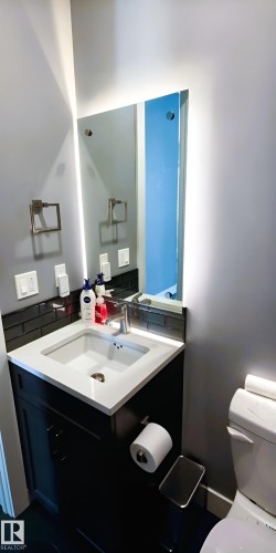 This bathroom features a contemporary vanity with a white countertop and an integrated sink, complemented by a sleek mirror with backlighting - 1781 Melrose Crescent, Edmonton, AB - Indoor Photo Showing Bathroom