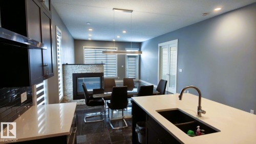The open-concept living space features a stone-clad fireplace and large windows, complemented by recessed lighting and a modern linear light fixture - 1781 Melrose Crescent, Edmonton, AB - Indoor With Fireplace