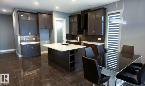 This kitchen features dark cabinetry, a white island countertop with an integrated sink, and dark tiled flooring - 1781 Melrose Crescent, Edmonton, AB - Indoor