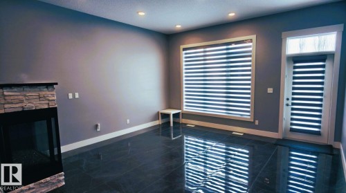 This living area features dark tiled flooring, a stone-accented fireplace, and recessed lighting - 1781 Melrose Crescent, Edmonton, AB - Indoor Photo Showing Other Room With Fireplace