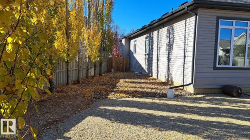 The property features a gravel side yard with a line of trees and a wooden fence - 1781 Melrose Crescent, Edmonton, AB - Outdoor