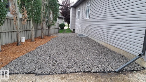 The property features a gravel side yard with a wooden fence and mature trees - 1781 Melrose Crescent, Edmonton, AB - Outdoor