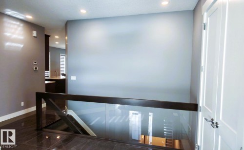 View of the interior featuring glossy tiled floors, a glass and dark wood railing, and a white interior door with a chrome handle - 1781 Melrose Crescent, Edmonton, AB - Indoor Photo Showing Other Room