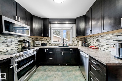 The kitchen features dark cabinetry, stainless steel appliances, a mosaic tile backsplash, and a window above the sink - 5418 17A Avenue, Edmonton, AB - Indoor Photo Showing Kitchen With Upgraded Kitchen