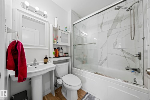 Bathroom featuring a pedestal sink, a toilet, and a bathtub with a clear glass sliding door - 5418 17A Avenue, Edmonton, AB - Indoor Photo Showing Bathroom