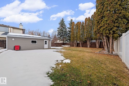 The property features a spacious yard with a mix of lawn and mature trees, alongside a detached structure with siding and a white door - 5418 17A Avenue, Edmonton, AB - Outdoor