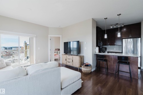 Open concept living area featuring dark hardwood floors, a kitchen with stainless steel appliances, and a balcony with an urban view - 402 3670 139 Avenue, Edmonton, AB - Indoor