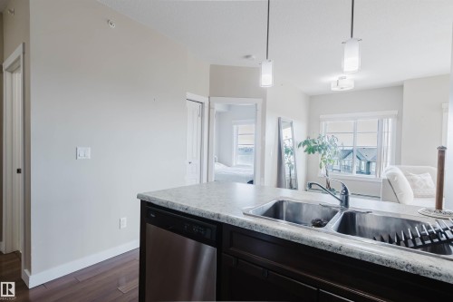 The kitchen features a double basin stainless steel sink with a chrome faucet, a dishwasher, dark wood cabinetry, and light-colored countertops - 402 3670 139 Avenue, Edmonton, AB - Indoor Photo Showing Kitchen With Double Sink