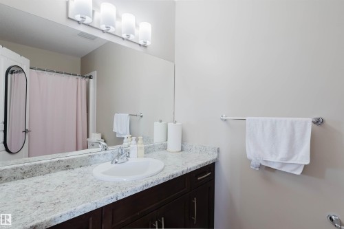 Bathroom featuring a spacious vanity with a light-colored speckled countertop, a single sink with a chrome faucet, and dark wood cabinetry - 402 3670 139 Avenue, Edmonton, AB - Indoor Photo Showing Bathroom