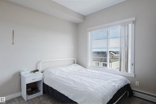The bedroom features a large window providing natural light and a view of surrounding rooftops - 402 3670 139 Avenue, Edmonton, AB - Indoor Photo Showing Bedroom