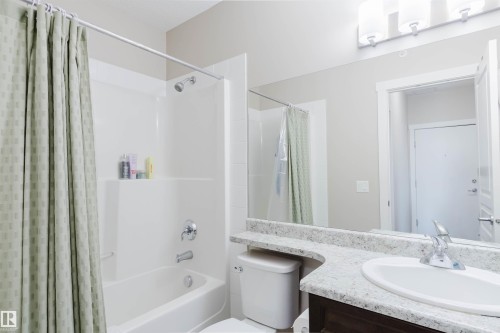 Bathroom featuring a shower/tub combination with chrome fixtures, a vanity with a white countertop and a single sink, and a large mirror - 402 3670 139 Avenue, Edmonton, AB - Indoor Photo Showing Bathroom