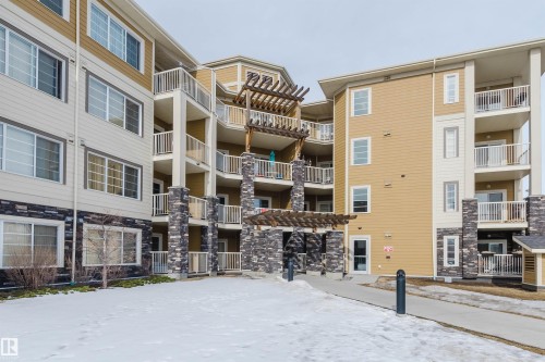The property features a multi-story building with a light-colored facade, contrasting with dark stone accents on the lower levels and support pillars - 402 3670 139 Avenue, Edmonton, AB - Outdoor With Balcony With Facade