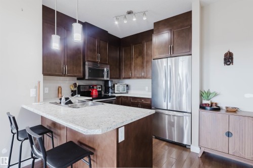 Kitchen featuring wood flooring, dark wood cabinetry, a light-colored countertop, and stainless steel appliances - 402 3670 139 Avenue, Edmonton, AB - Indoor Photo Showing Kitchen With Stainless Steel Kitchen With Double Sink