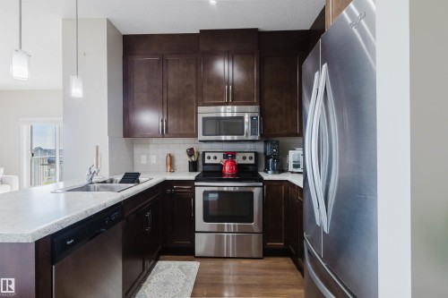 The kitchen features dark wood cabinetry, stainless steel appliances, and light-colored countertops - 402 3670 139 Avenue, Edmonton, AB - Indoor Photo Showing Kitchen With Stainless Steel Kitchen With Double Sink With Upgraded Kitchen