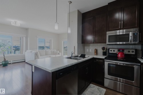 The kitchen features dark wood cabinetry, stainless steel appliances, and a light-colored countertop - 402 3670 139 Avenue, Edmonton, AB - Indoor Photo Showing Kitchen With Stainless Steel Kitchen With Double Sink