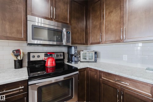The kitchen features dark wood cabinetry, white subway tile backsplash, and light-colored countertops - 402 3670 139 Avenue, Edmonton, AB - Indoor Photo Showing Kitchen