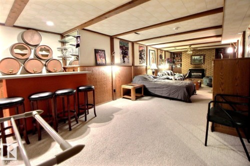Spacious room featuring carpeting, exposed wood beams on the ceiling, a bar area with stools, and an exposed brick wall with a fireplace - 243 Lynnwood Way, Edmonton, AB - Indoor Photo Showing Other Room