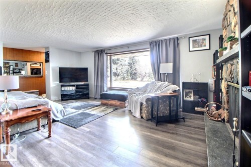 Living area featuring light-toned flooring, a large window with grey drapes, and a fireplace with a stone facade - 243 Lynnwood Way, Edmonton, AB - Indoor