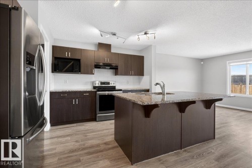 The kitchen features dark wood cabinetry, stainless steel appliances, a white tile backsplash, and a central island with a granite countertop and sink - 17023 38 Street Nw, Edmonton, AB 