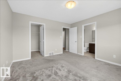 This bedroom features light grey carpeting, light grey painted walls, and white trim throughout. With in-suite bathroom and walk-in closet - 17023 38 Street Nw, Edmonton, AB 