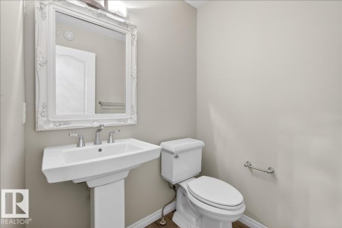 This bathroom features a white pedestal sink with a chrome faucet, a toilet, and a decorative white framed mirror - 17023 38 Street Nw, Edmonton, AB 