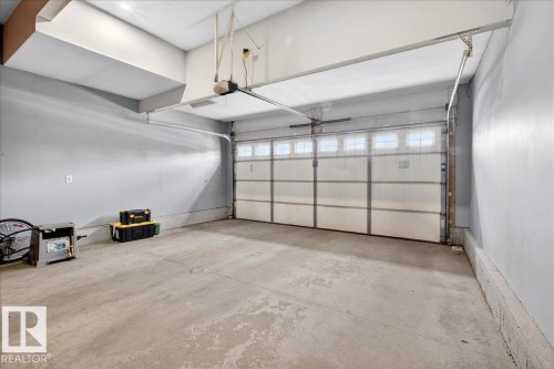The property features a garage with a concrete floor, light gray walls, and a white garage door with upper window panels - 17023 38 Street Nw, Edmonton, AB 