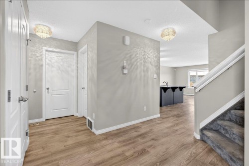 Entryway featuring light wood-look flooring, neutral wall paint, and a carpeted staircase - 17023 38 Street Nw, Edmonton, AB 