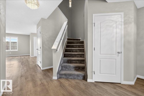 Entryway featuring wood-look flooring, a carpeted staircase, and light gray painted walls - 17023 38 Street Nw, Edmonton, AB - Indoor Photo Showing Other Room