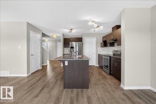 The kitchen features a central island with a granite countertop and an undermount sink, dark wood cabinetry, and stainless steel appliances - 17023 38 Street Nw, Edmonton, AB 