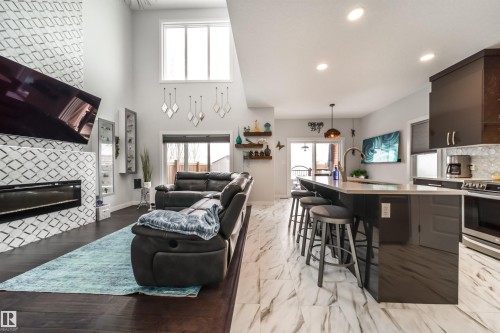 This open-concept living space features high ceilings, large windows, and dark hardwood flooring in the living area - 3514 49 Avenue, Beaumont, AB - Indoor Photo Showing Living Room With Fireplace